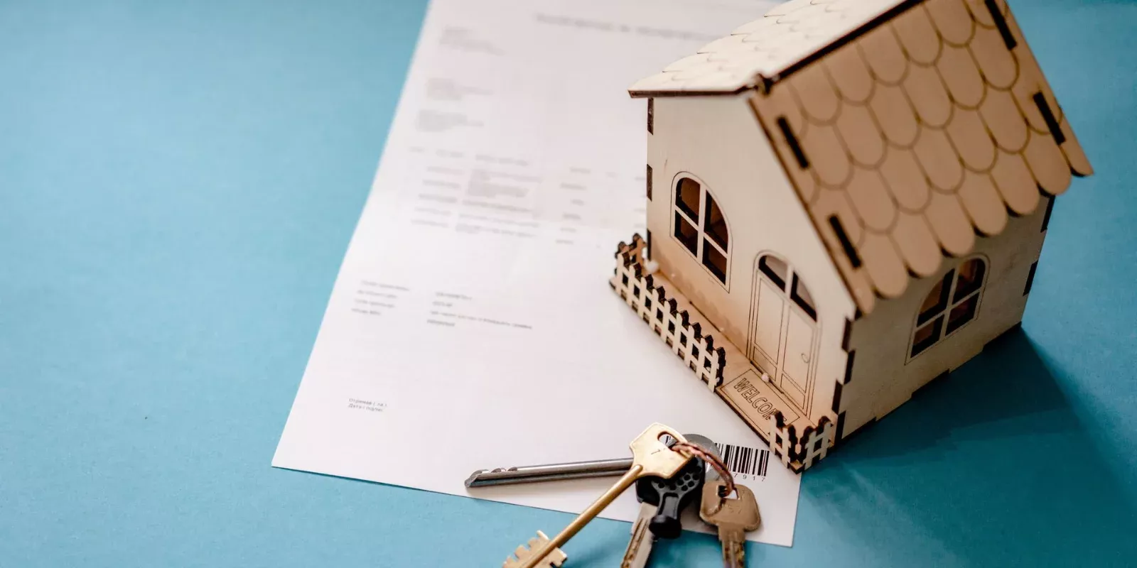 Casa en miniatura de madera junto a unas llaves y un contrato sobre una mesa