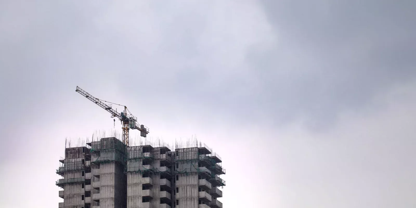 Torre residencial en construcción con grúa bajo un cielo nublado