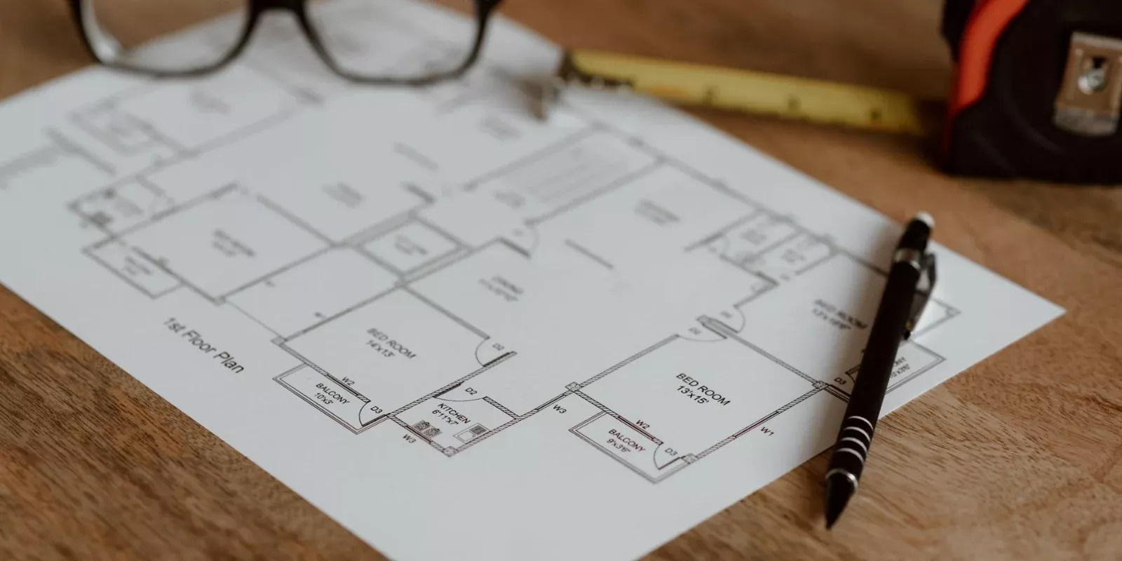 Plano de una vivienda sobre una mesa junto a una regla, un lápiz y unas gafas