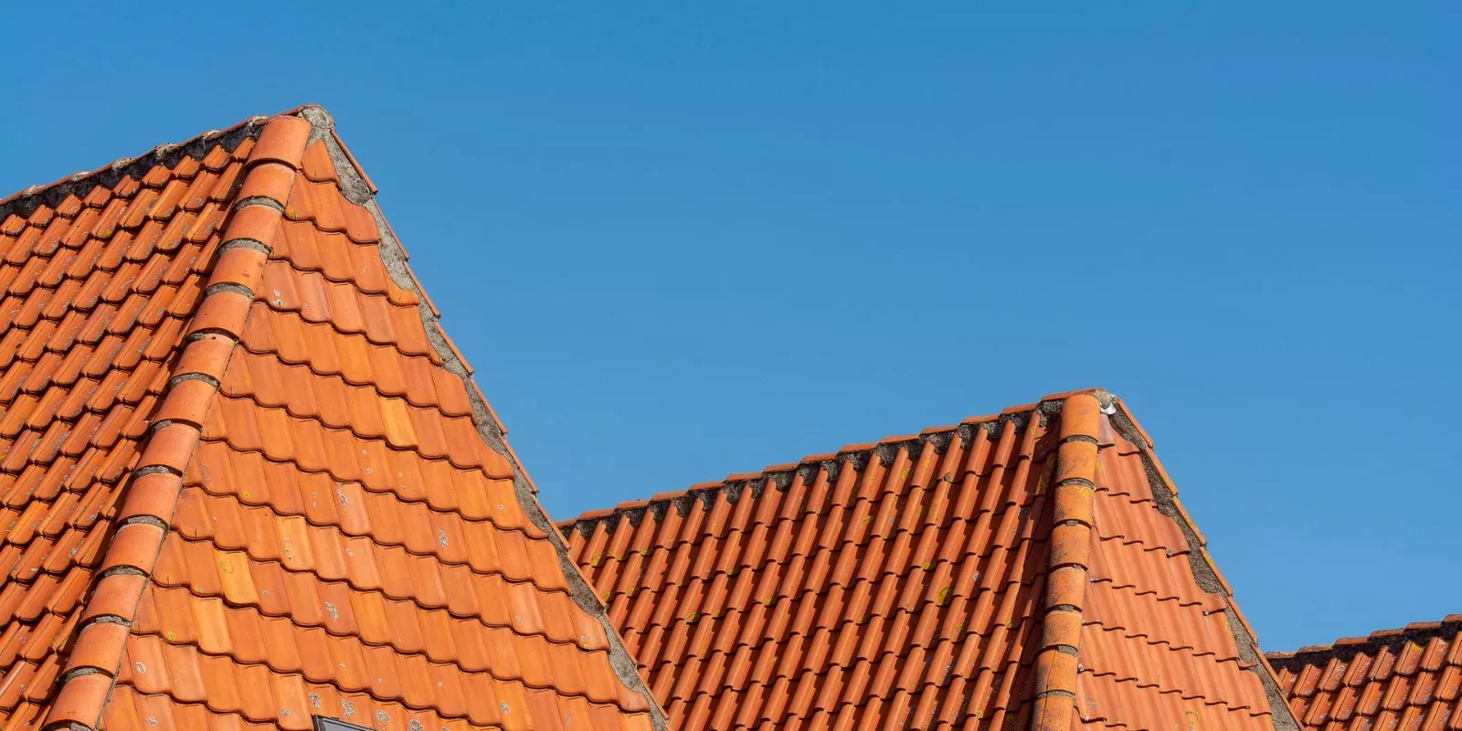 Techo de tejas de una vivienda recortado contra un cielo azul despejado